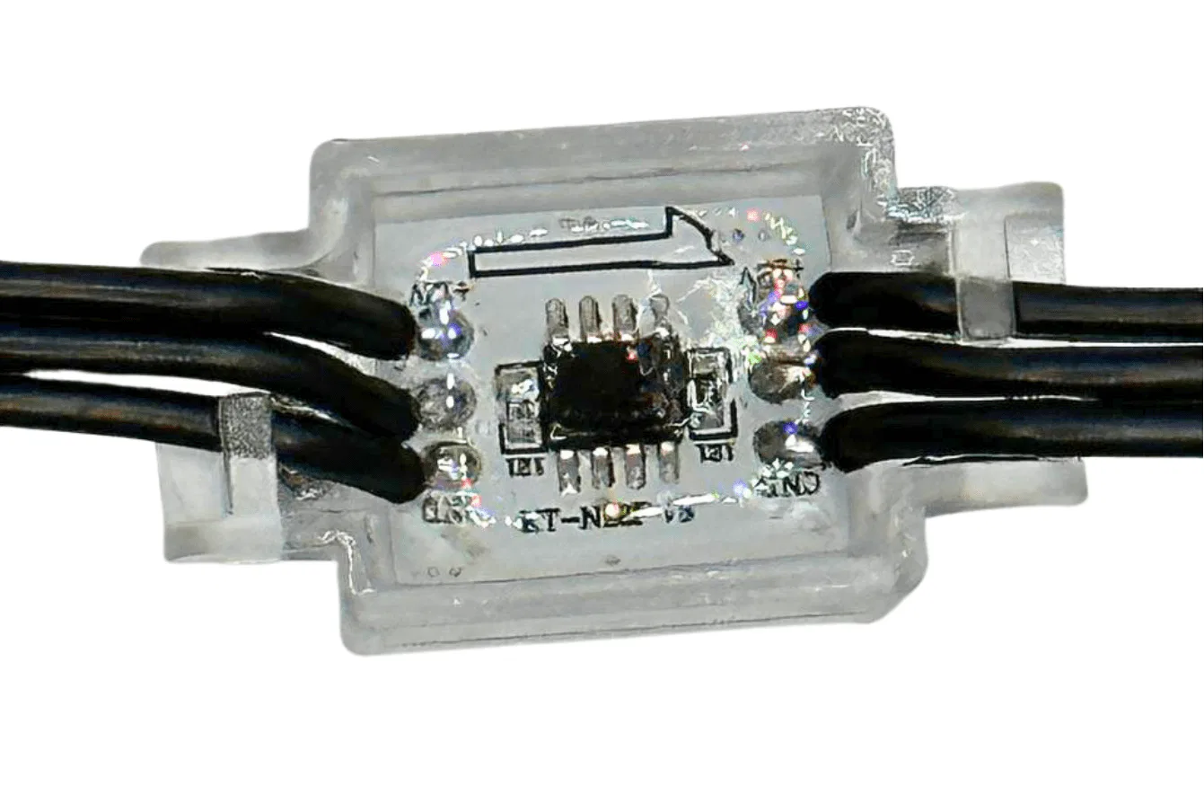 Close-up of an electronic component encased in clear plastic, showing a small circuit board with a microchip and six black wires connected to it on both sides, with a black arrow printed on the casing.