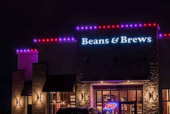A Beans & Brews coffee shop at night, with purple and red lights along the roof and a bright OPEN neon sign in the window.
