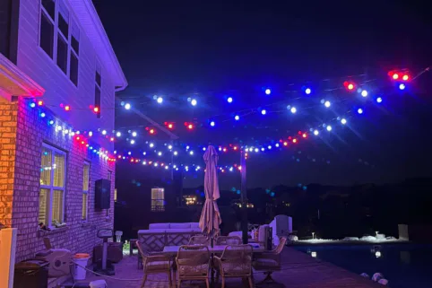 A patio with a table and chairs and a pool at night.